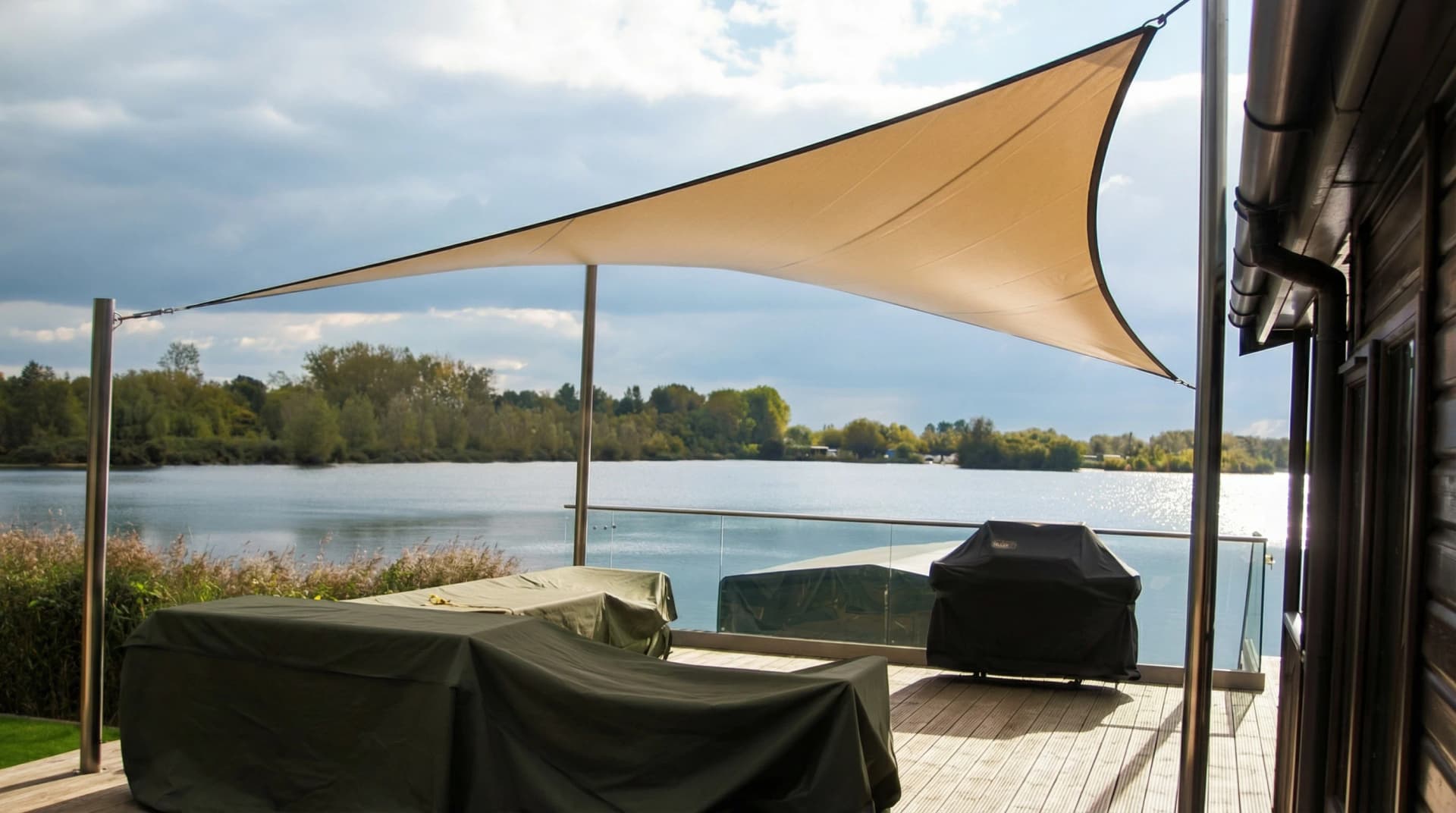 Beigt segelduk-solsegel spännt med sjöutsikt vid träaltan och skyddad trädgårdsmöbel