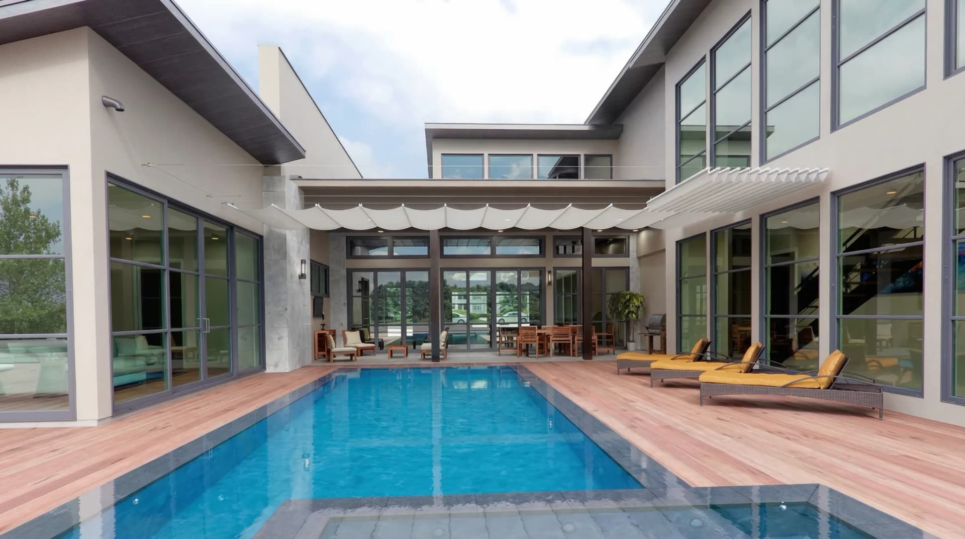 Vajersolskydd med beige markis spännt på stålpergola vid lyxvilla med pool och solstolar